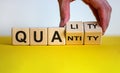 Quality over quantity. Hand turns cubes and changes the word `quantity` to `quality`. Beautiful yellow table, white background