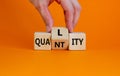 Quality over quantity symbol. Businessman turns cubes and changes the word `quantity` to `quality`. Beautiful orange table, or