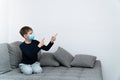 A quarantine boy sits in a mask on a sofa and points his hands to a place for text. Epidemic of coronavirus COVID19