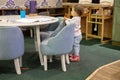 Quarantine with children at home. a little cute toddler is standing behind a children`s small low table and child seats