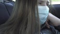 Quarantine concept.Bored Sick littele girl in mouth mask rides in the back seats of a car. Sad girl in protective medical mask