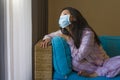 Quarantine and home lockdown - young beautiful stressed and worried Asian Chinese woman in pajamas on couch in surgical mask