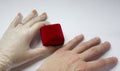 Quarantined wedding.coronavirus wedding.hand in a medical glove with a wedding ring on a white background next to a red