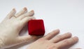 Quarantined wedding.coronavirus wedding.hand in a medical glove with a wedding ring on a white background next to a red