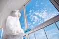 Quarantined woman in mask on self-isolation in apartment looks out balcony window blue sky and clear air
