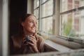 Quarantined young woman smiling drinking coffee and daydreaming looking out at empty streets Royalty Free Stock Photo