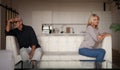 Quarrel in a mature family. Senior husband and wife are sitting on opposite sides of the sofa in the interior of the apartment. Royalty Free Stock Photo