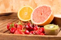 quarter of orange a grapefruit half kiwi with cherry and strawberry in a wooden tray Royalty Free Stock Photo