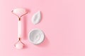 Quartz facial massager, moisturizer cream smear and jar on pink background with copy space, top view. Trendy skin care