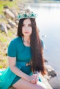 Queen in a green dress with a train and emerald eorone. Sexy brunette on the lake. Girl on the stones with