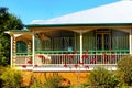 Queensland house with ornate metal bars on wrap around porch, metal roof and poinsettas growning in front
