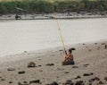 Boy fishing in the shore of a river, sitting in an old rubber wheel