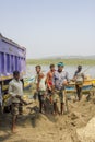 Indian men load sand into a truck with shovels on the background of the river