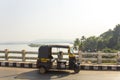 Indian rickshaw taxi stands on a bridge against the background of the river and green palm juggles