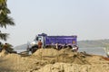 Indian workers load sand into a white purple truck against the backdrop of the river