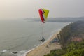Paraglider on a yellow parachute and a helmet flies over the beach with people and the ocean against