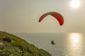 A tandem of paragliders on a red-yellow parachute flies over the ocean with a sun path in the Royalty Free Stock Photo