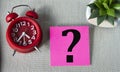 Question mark on note sheet on gray background with alarm clock and cactus Royalty Free Stock Photo