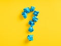 Question mark symbol made out of blue crumpled papers on yellow background. Query, problem, dilemma, confusion, mystery or
