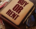 The question to Buy or Rent typed on a cover of book, eyeglasses and pen. analysis of real estate market and personal Royalty Free Stock Photo