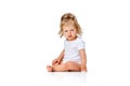 Questioning funny face. Cute, beautiful little girl, toddler sitting on floor with grimacing face against white studio