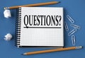 QUESTIONS? - word in a white notebook on a blue background with pencils, paper clips