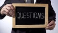Questions written on blackboard, business person holding sign, FAQ, advice