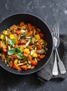 Quick ratatouille in a cast iron skillet on a dark background, top view. Steamed vegetables - vegetarian food