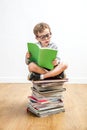 Quiet bookworm schoolboy seated on top of many books, indoor