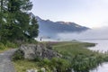 The quiet douglas tree woods on the shore of the lake of Silvaplana in the Engadin valley at sunrise with the fog over the water Royalty Free Stock Photo