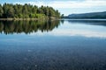 A quiet peaceful summer morning with view over crystal clear calm lake with pebbles in the bottom and forest reflected