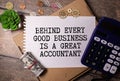 Quote Behind Every Good Business Is A Great Accountant handwritten on notebook page next to calculator and pen