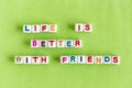 Quote `Life is better with friends` made out of colorful beads on lime background