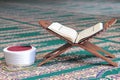 Quran, imam fez and rosary beads on a wooden stand in mosque.