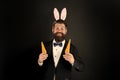 Rabbit bringing Easter carrots. Easter rabbit black background. Bearded man hold carrots. Happy businessman wear rabbit