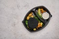 Rabbit cutlet in black breading in baby potatoes, spinach and mushrooms in black plastic container on light background