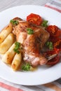 Rabbit leg roasted with apples and tomatoes on a plate closeup.