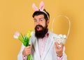 Rabbit man in bunny ears with flowers and basket eggs. Easter celebration concept. Bearded man in suit with Spring