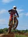 Racer on a cross-country motorcycle in sports equipment in flight after jumping on a springboard, against the blue sky