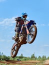 Racer on a cross-country motorcycle in sports equipment in flight after jumping on a springboard, against the blue sky