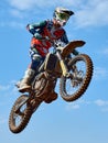 Racer on a cross-country motorcycle in sports equipment in flight after jumping on a springboard, against the blue sky