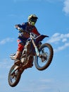 Racer on a cross-country motorcycle in sports equipment in flight after jumping on a springboard, against the blue sky