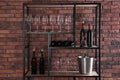 Rack with bottles of wine and glasses near brick wall Royalty Free Stock Photo
