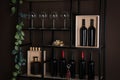 Rack with bottles of wine and glasses near brown wall Royalty Free Stock Photo