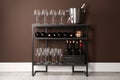 Rack with bottles of wine and glasses near brown wall Royalty Free Stock Photo