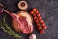 Rack of lamb on a cutting board with rosemary, pepper peas, red tomatoes on a twig on a concrete dark background. BBQ cooking. Royalty Free Stock Photo