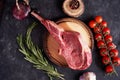 Rack of lamb on a cutting board with rosemary, pepper peas, red tomatoes on a twig on a concrete dark background. BBQ cooking. Royalty Free Stock Photo