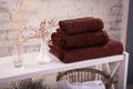 Rack with a stack of three brown color towels and baskets with clean white towels and toilet decor near a brick wall. Shelf with Royalty Free Stock Photo