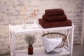 Rack with a stack of three brown color towels and baskets with clean white towels and toilet decor near a brick wall. Shelf with Royalty Free Stock Photo