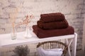 Rack with a stack of three brown color towels and baskets with clean white towels and toilet decor near a brick wall. Shelf with Royalty Free Stock Photo